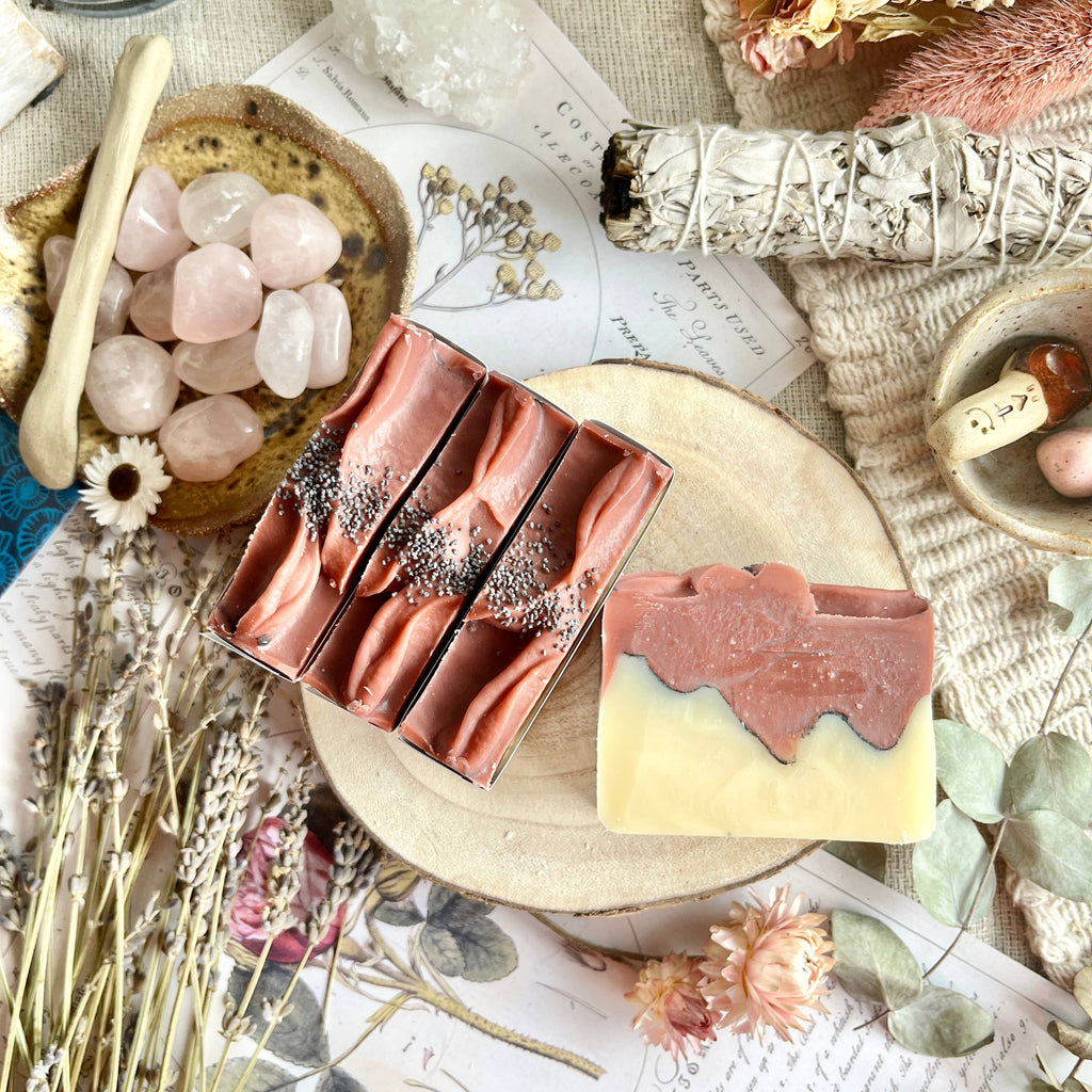 Three bars of soap on a wooden board with decorative elements like flowers and crystals.