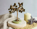 Decorative stone tree on a wooden base with a candle and flowers in the background