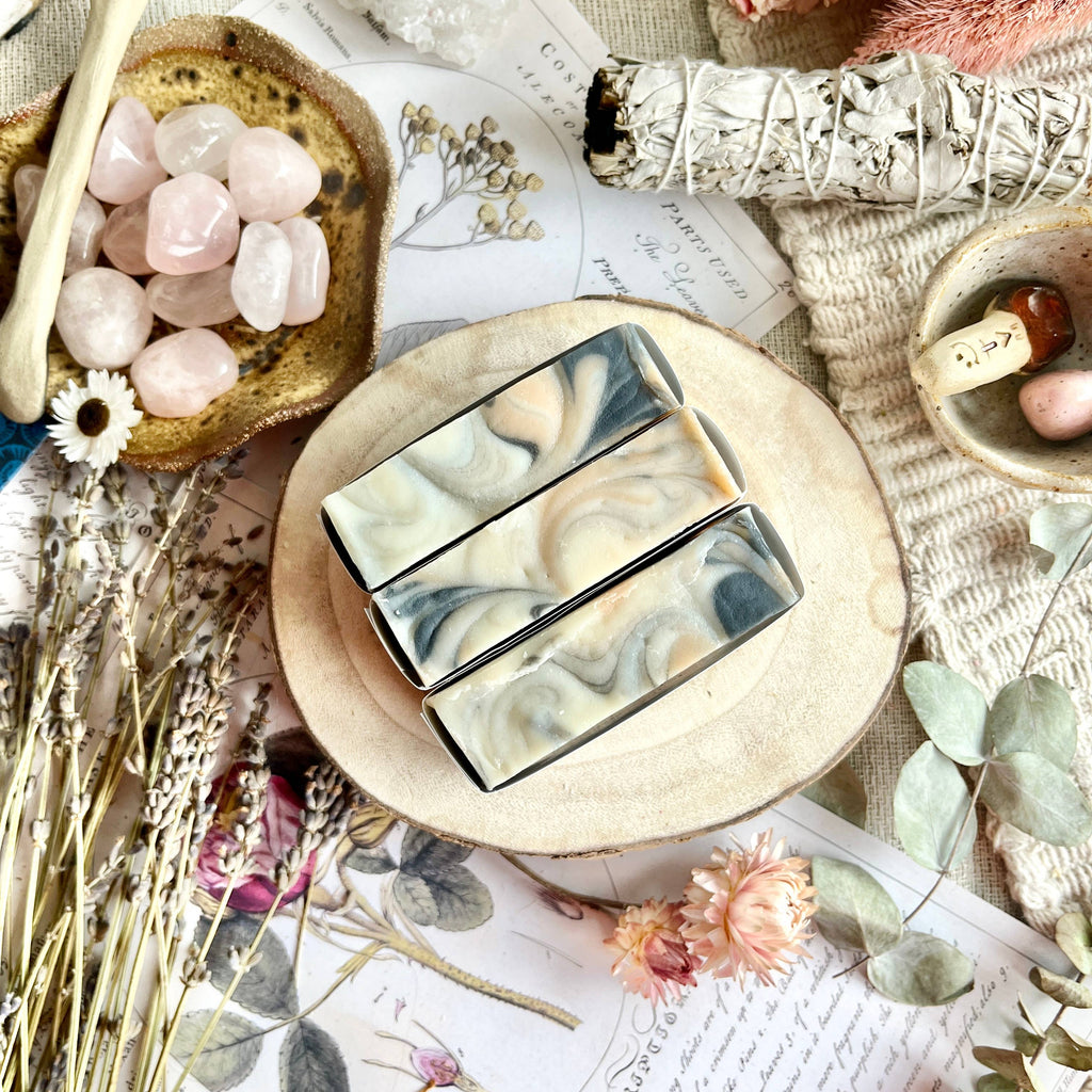 Two marbled soap bars on a wooden stand with decorative elements like stones and flowers.
