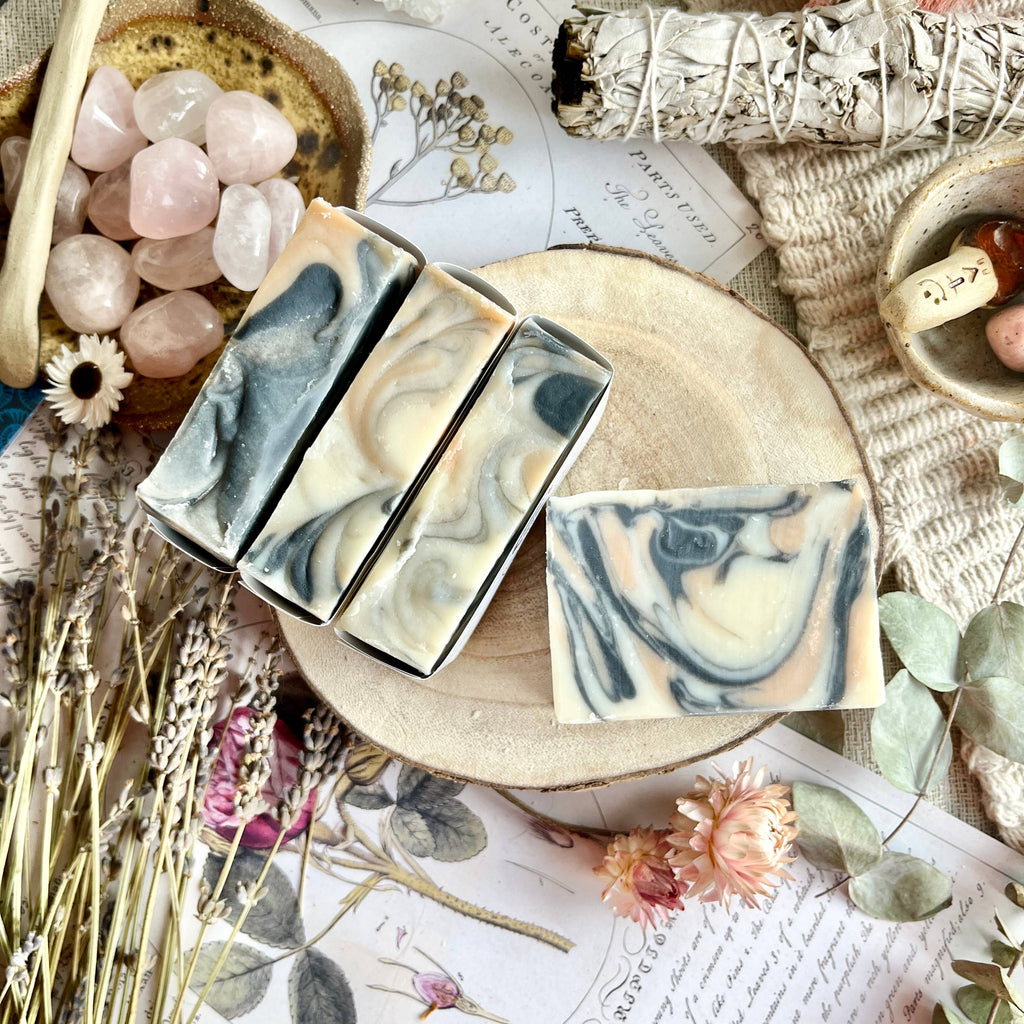 Three soap bars with marble pattern on a wooden board with decorative elements like flowers and stones.