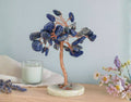 Decorative stone tree on a wooden surface with a candle and flowers in the background.